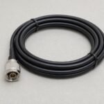Coiled black coaxial cable with a silver connector on a clean gray surface
