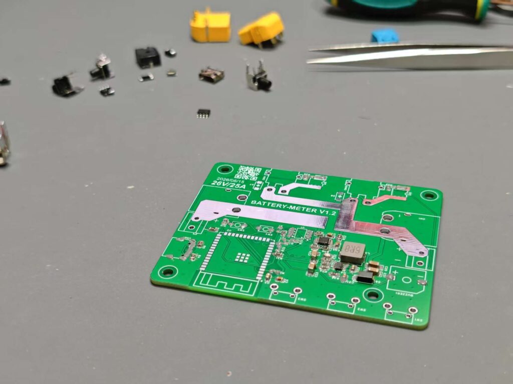 Partially assembled green battery meter PCB on a workbench with shunt and power traces visible.