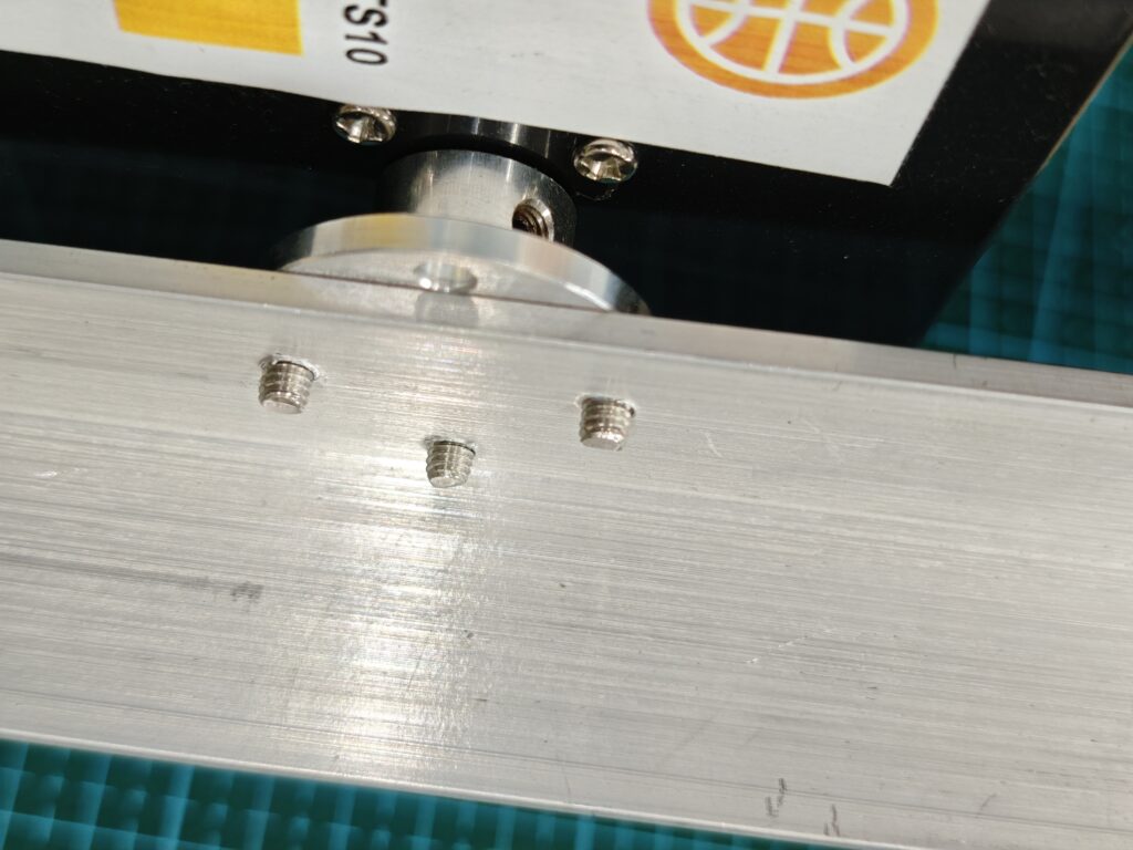 Close-up rear view of a metal flange coupling mounted to a thread tapped aluminum angle bar for an amateur radio antenna rotator, secured with three screws (no nuts used), connecting to the elevation (EL) motor to control the antenna's tilt.