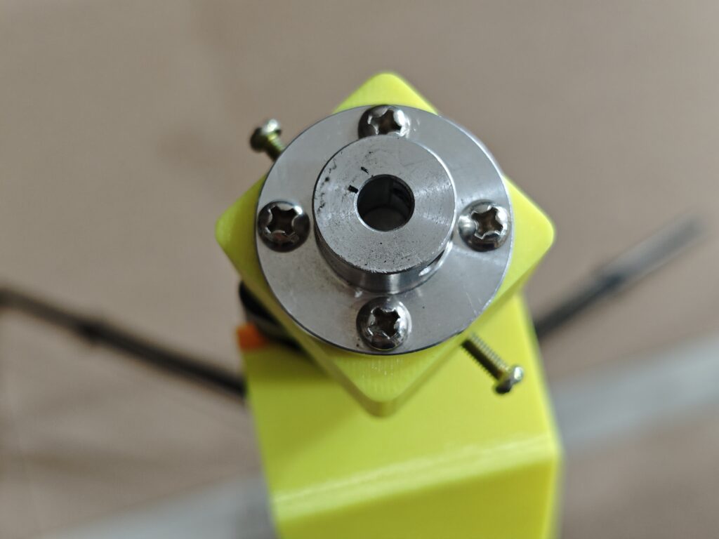 Close-up shot of a 3D-printed yellow adapter mounting a metal flanged coupler to a tripod, secured by four screws, with the coupler's bore designed to connect to the shaft of azimuth (AZ) motor.
