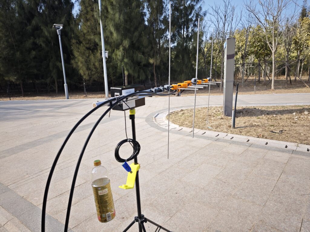 Outdoor field setup of a DIY amateur radio antenna rotator system. A 1.5-liter water bottle serves as a rear counterweight, balanced by a thin lead wire attached to the end of the PVC pipe, critical for relieving stress on the elevation (EL) motor and gears to prevent damage during antenna movement.