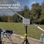 Homemade AZ/EL antenna rotator with gray controller enclosure, aluminum arm, yellow 3D printed bracket, Yagi antenna, tripod mount, water bottle counterweight, and an ICOM IC-705-style radio on the table in a portable ham radio satellite setup.